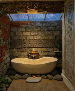 bañera en una habitación con pared de piedra en Honeymoon Green Villa, en Ubud