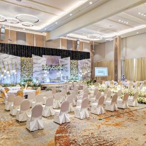 un salón de banquetes con sillas blancas y un escenario en HARRIS Hotel Batam Center en Batam Centre