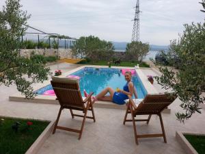 a woman sitting next to a swimming pool at Holiday house with a swimming pool Bol, Brac - 11016 in Bol