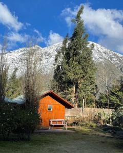a cabin with a bench in front of a snow covered mountain at Cabañas Los Olmos in San José de Maipo