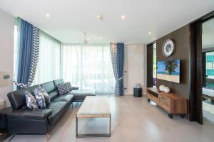 sala de estar con sofá de cuero negro y TV en Karon Sea View Beach Apartment, en Karon Beach