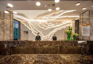 two men standing at a counter in a lobby with a cloud mural at Muong Thanh Luxury Saigon Hotel in Ho Chi Minh City
