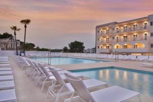 a hotel pool with white chairs and a building at Barceló Aguamarina in Cala d´Or