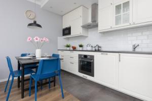 a kitchen with white cabinets and a table with blue chairs at Warsaw Ursynów Apartment with Balcony by Noclegi Renters in Warsaw