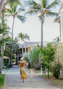 a woman and child walking down a sidewalk with palm trees at Hotel Le Recif, Ile de la Reunion in Saint-Gilles-les-Bains