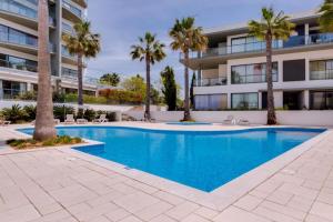 a swimming pool in front of a building with palm trees at Cavalo Branco Portugal in Quarteira