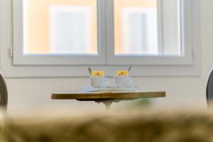 two coffee cups on a table in front of two windows at L'ISLE D'OR - LES AMANDIERS - 3 étoiles - 1er étage in LʼIsle-sur-la-Sorgue