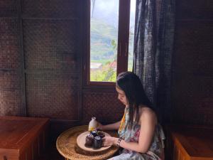 Goong House في سابا: امرأة تجلس على طاولة مع كوب من القهوة