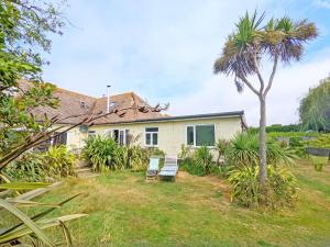 a house with two chairs and a palm tree at Coastal - Wittering in West Wittering