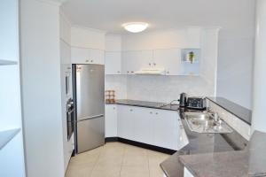 Una cocina con gabinetes blancos y un refrigerador de acero inoxidable. en Ocean Shores Apartment 17 - Bring you own linen., en South West Rocks