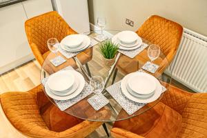 a glass table with chairs and plates and wine glasses at Campbell Park Apartment - City Centre - Free Parking, Balcony, Super-Fast Wifi and Smart TV with Netflix by Yoko Property in Milton Keynes