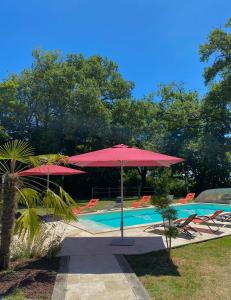 a pool with two umbrellas and chairs and a swimming pool at Maison D'hôtes Sainte-Marie in Mirande