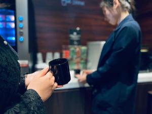 una mujer sosteniendo una taza de café delante de un mostrador en Hotel Hulaton Fukuokahakata en Fukuoka