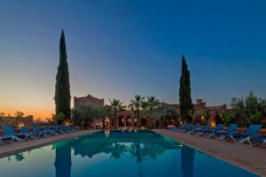 a swimming pool with chairs and palm trees and the sunset at Kasbah Angour in Tahannout