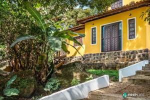 Una casa amarilla con un árbol delante. en Chalés da Libélula, en Ilhabela