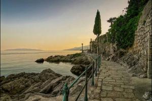 a stone path next to the water with a tree at Apartments Villa Dinka in Opatija