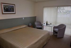 1 Schlafzimmer mit einem Bett, 2 Stühlen und einem Tisch in der Unterkunft Shortland Court Motel in Thames