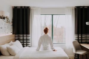 une femme assise sur un lit donnant par la fenêtre dans l'établissement Hôtel Château Joliette, à Joliette