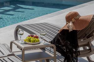 une femme assise sur une chaise avec un bol de fruits et des verres à vin dans l'établissement Casa D'Oro Suites by Estia 'Adults Only', à Panormos Rethymno