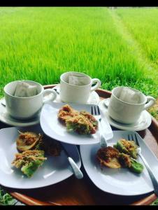 a table with plates of food and cups and a field at GumiBali Villa in Tirtagangga
