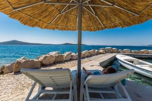 a woman laying in a chair under an umbrella on a beach at Secluded fisherman's cottage Cove Donje More, Pasman - 11515 in Tkon