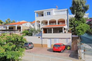 uma casa branca com um carro vermelho estacionado em frente dela em Apartments by the sea Seget Vranjica, Trogir - 13771 em Trogir