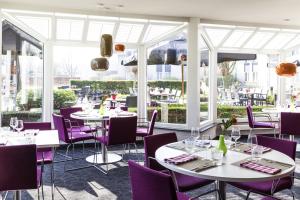 un restaurante con mesas blancas y sillas moradas en Novotel Breda, en Breda