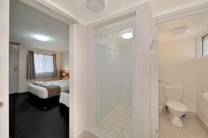 a bathroom with a shower and a toilet and a bed at Oscar Motel in Bundaberg