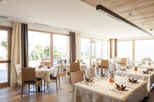 um restaurante com mesas e cadeiras brancas e janelas em Family Home Alpenhof em Maranza