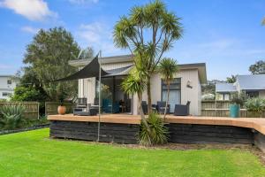 a house with a deck with a palm tree at Bayside Beauty - Matapouri Holiday Home in Matapouri