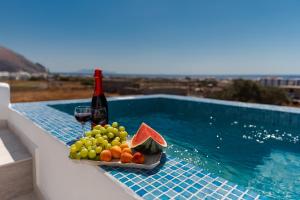 a tray of fruit and a bottle of wine next to a swimming pool at The Tree Houses Santorini in Perissa