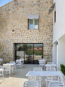 a patio with white tables and chairs next to a stone wall at Hôtel De Porticcio in Porticcio