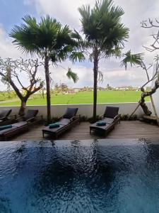 a pool with chaise lounges next to palm trees at The Kd Suites & Coffee Shop in Munggu