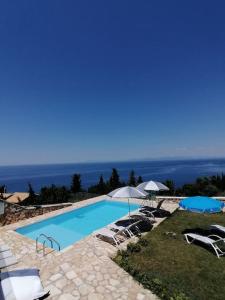 a swimming pool with chairs and umbrellas and the ocean at Villa ioli at the sea breathtaking view & sunset in Agios Nikitas