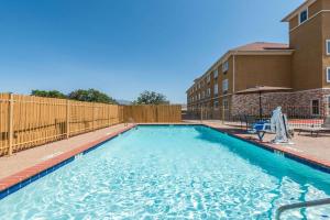 a swimming pool with a fence and a building at Days Inn & Suites by Wyndham Cleburne TX in Cleburne