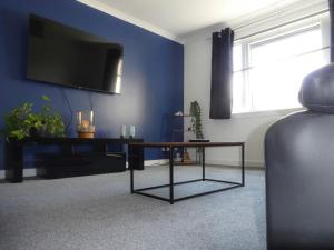 uma sala de estar com uma mesa e uma televisão numa parede azul em Dumfries Apartment em Dumfries