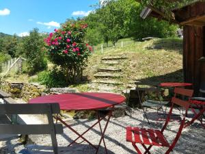 a red table and chairs on a patio with flowers at LES REPAIRES in Nans-sous-Sainte-Anne