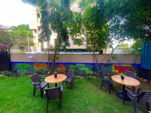 two tables and chairs in a yard with graffiti on a wall at Bern Hostel By Vibe Village in Pune