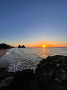 un coucher de soleil sur une plage avec des rochers et l'océan dans l'établissement Flat Siriguela, à Fernando de Noronha