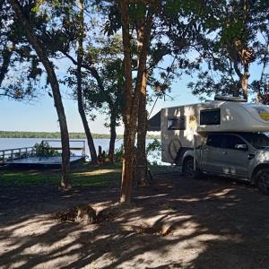 uma caravana estacionada ao lado de um lago com um barco em Camping Mirante dos Golfinhos em Cananeia