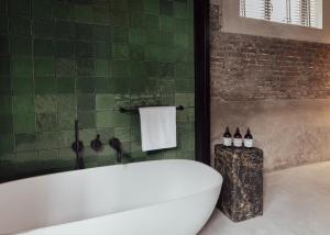 a bathroom with a white tub and a green tiled wall at Cousins Boutique Hotel in Maastricht
