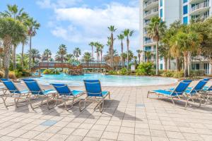 una piscina en el complejo con sillas azules y palmeras en Spectacular Sunsets 5 star Resort Condo Across from Beach Sleep 6 Private Shuttle, en Destin