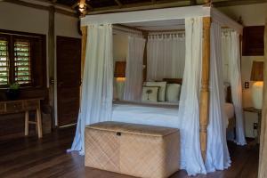 a bedroom with a canopy bed with a ottoman in it at Filha Da Lua Ecolodge in Pipa