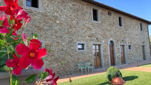 une maison en pierre avec des fleurs rouges devant elle dans l'établissement Villa Gosparini, à Lisciano Niccone
