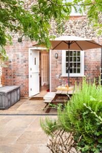 a patio with an umbrella in front of a brick building at No. 4 Back Lane - Norfolk Cottage Agency in Burnham Market