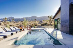 a swimming pool with people sitting on chairs next to a house at Amaru Muru - Luxury Retreat with Pool/Hot Tub/Yoga in Joshua Tree