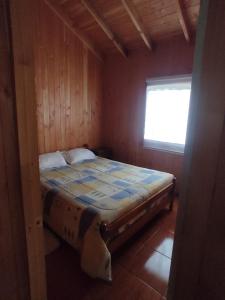 Cama en habitación de madera con ventana en Cabaña Los Maquis en Licán Ray