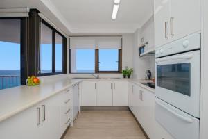 a white kitchen with white cabinets and windows at Carool Holiday Apartments in Gold Coast