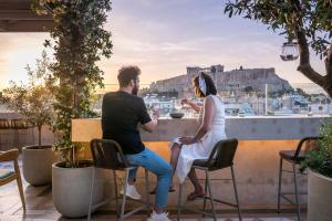 a man and woman sitting on a balcony with a view of the acropolis at Niche Hotel Athens in Athens