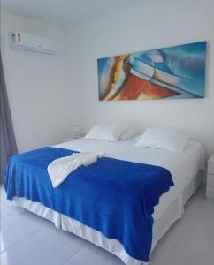 Una cama con una manta azul y una pintura en la pared en Casa De Verão, en Arraial d'Ajuda